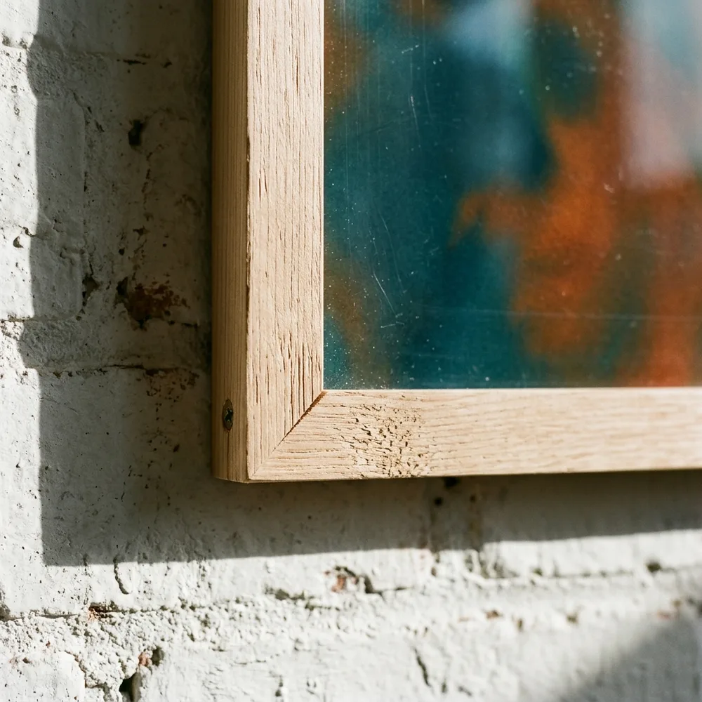 Mitred corner of a natural wood frame, the sheet running edge to edge under the plexiglass